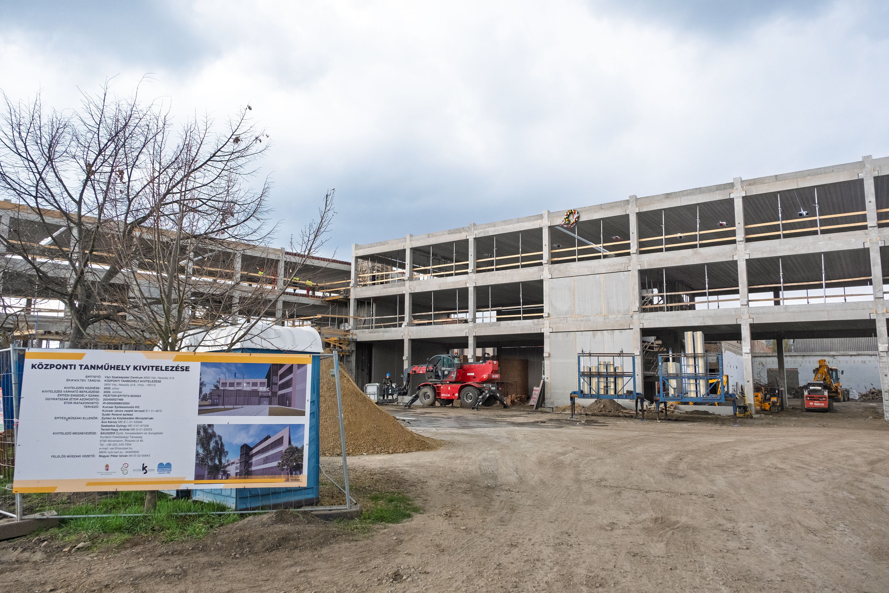 Vszc építkezés Bokrétaünnepség: a szerkezetkész vasbeton épület homlokzatán ott van már a bokréta, előtérben az udvar és az építkezés plakátja