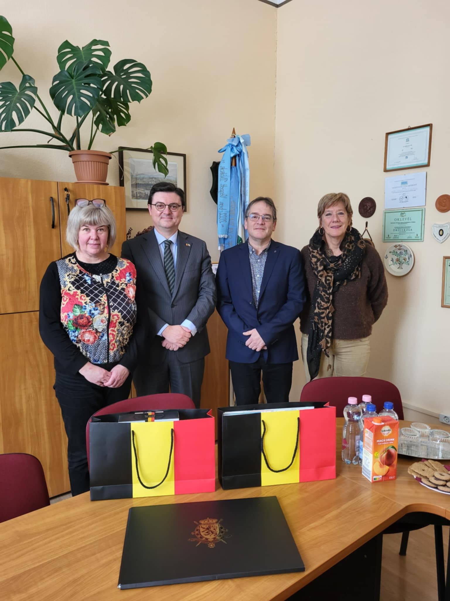 Az igazgatónő és a belga vendégek állnak, előttük egy asztalon belga zászlós zacskók