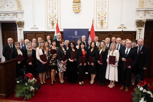 Csoportkép a díjazottakkal, miniszterrel, stb. Háttérben magyar zászlók, címer, előtérben állnak az emberek, tartják az oklevelüket