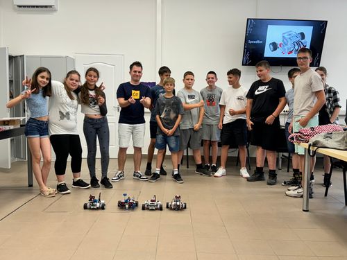 A 2024-es Pályaorientációs tábor résztvevőinek csoportképe, A gyerekek a segítőkkel együtt állnak a DKA terem aulájában, előttük lego robotok a földön